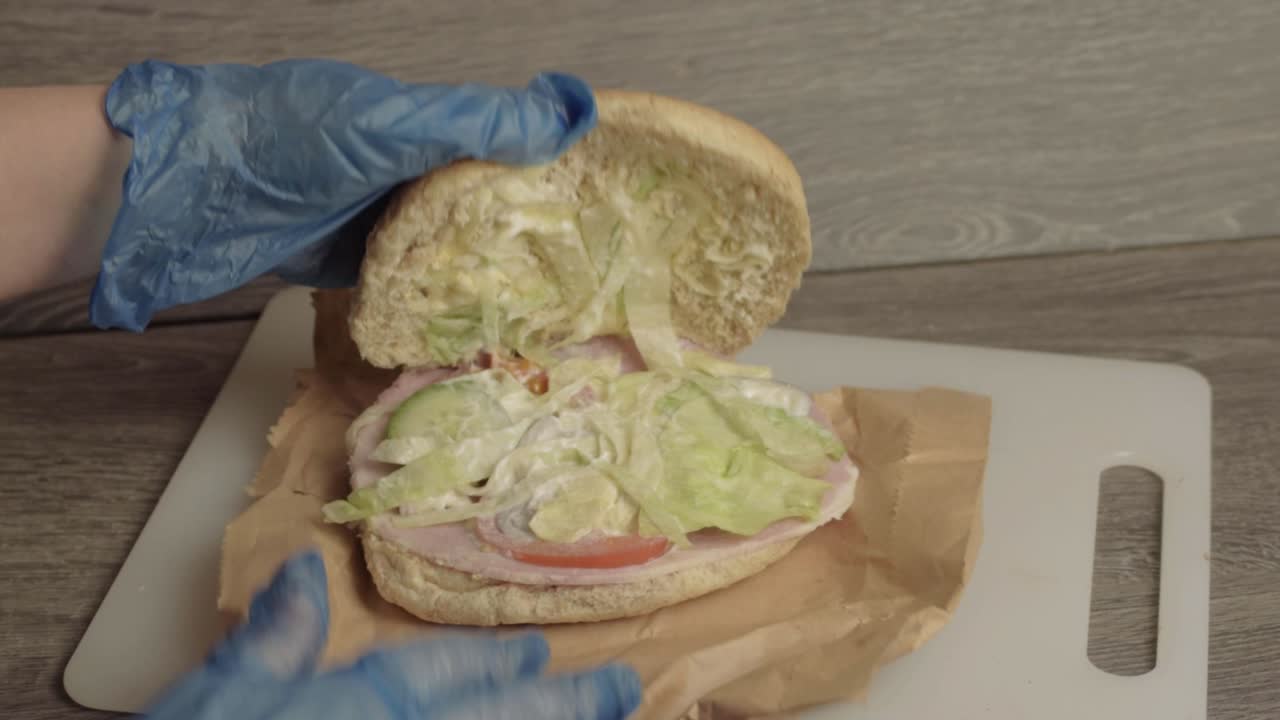 Mani che preparano un sandwich con insalata e guanti igienici, campo largo