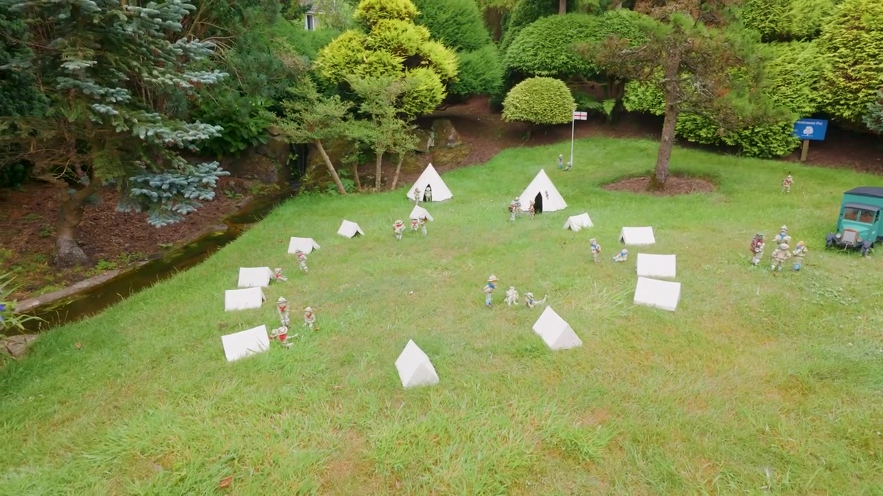 Modelcampingplads ved Godshill Model Village set i et langsomt kredsløb, der viser miniaturetelte, campister og et lille køretøj blandt velplejede græsplæner og havebuske.