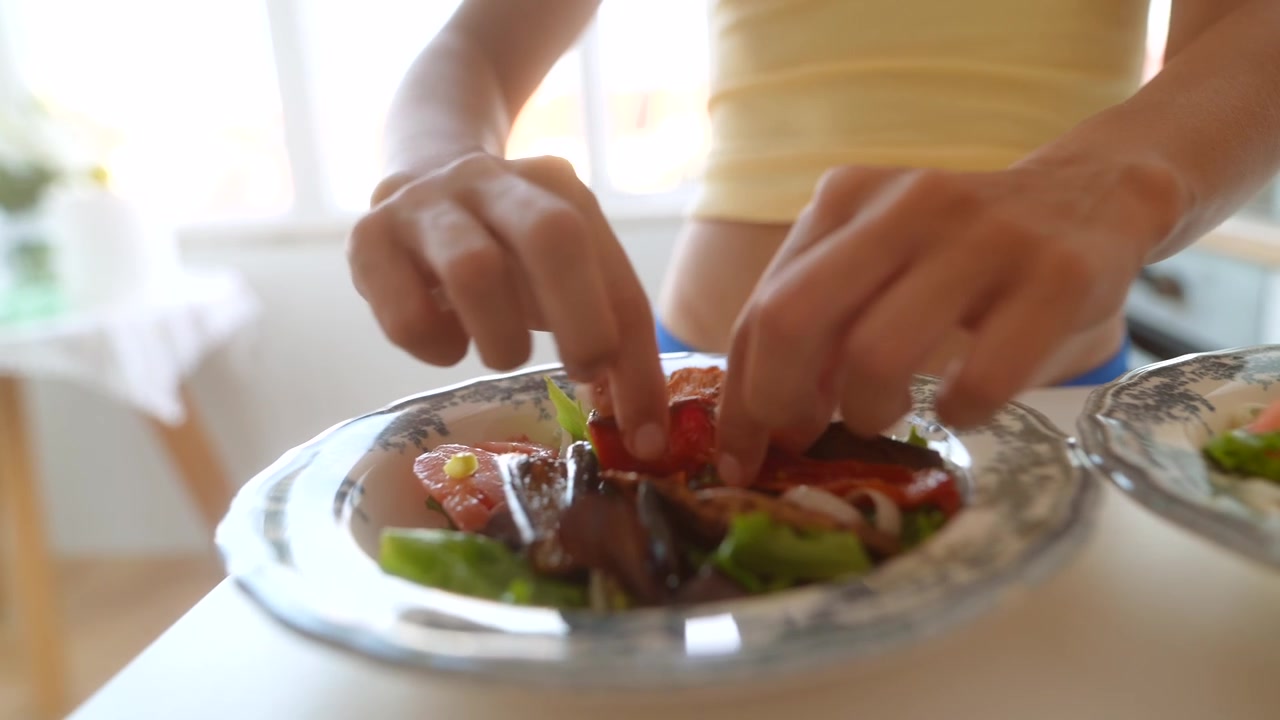 Mani di donna che aggiungono verdure arrostite a una ciotola di insalata sana