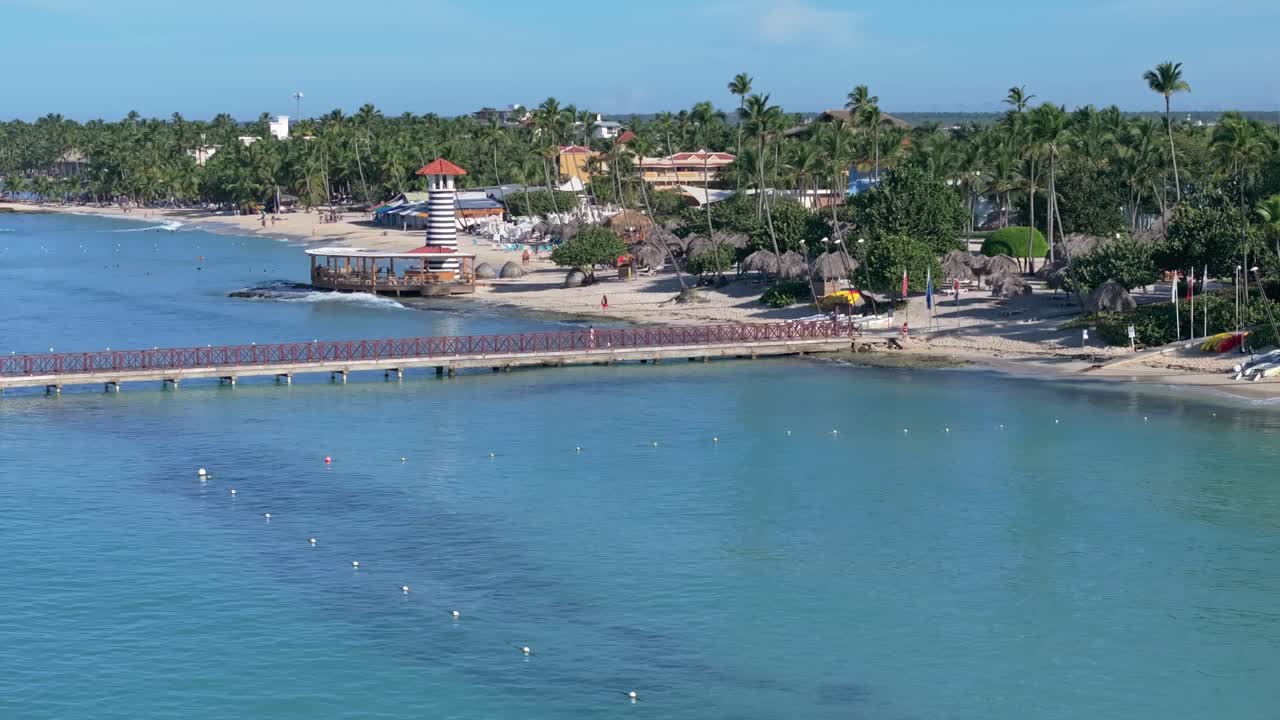 Aerial view overlooking turquoise waters, pier, and lighthouse at Dominicus Beach, Dominican Republic.Pan right, above shot