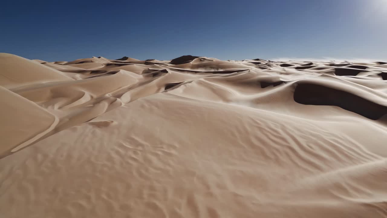 Aerial video of vast desert dunes under a clear blue sky, showcasing smooth, undulating sand