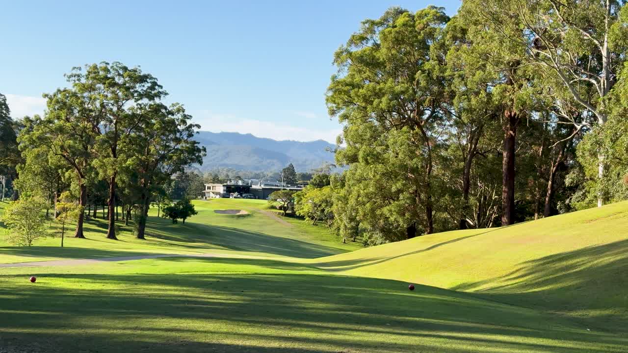 A tranquil golf course with lush greenery and distant mountains under clear blue skies, captured in a smooth panoramic motion