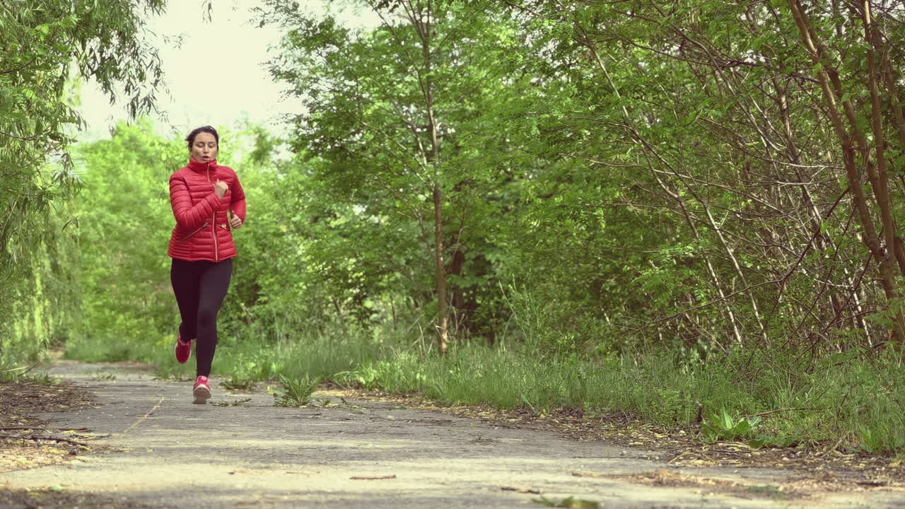 Active woman jogging on a forest path wearing a red sports jacket