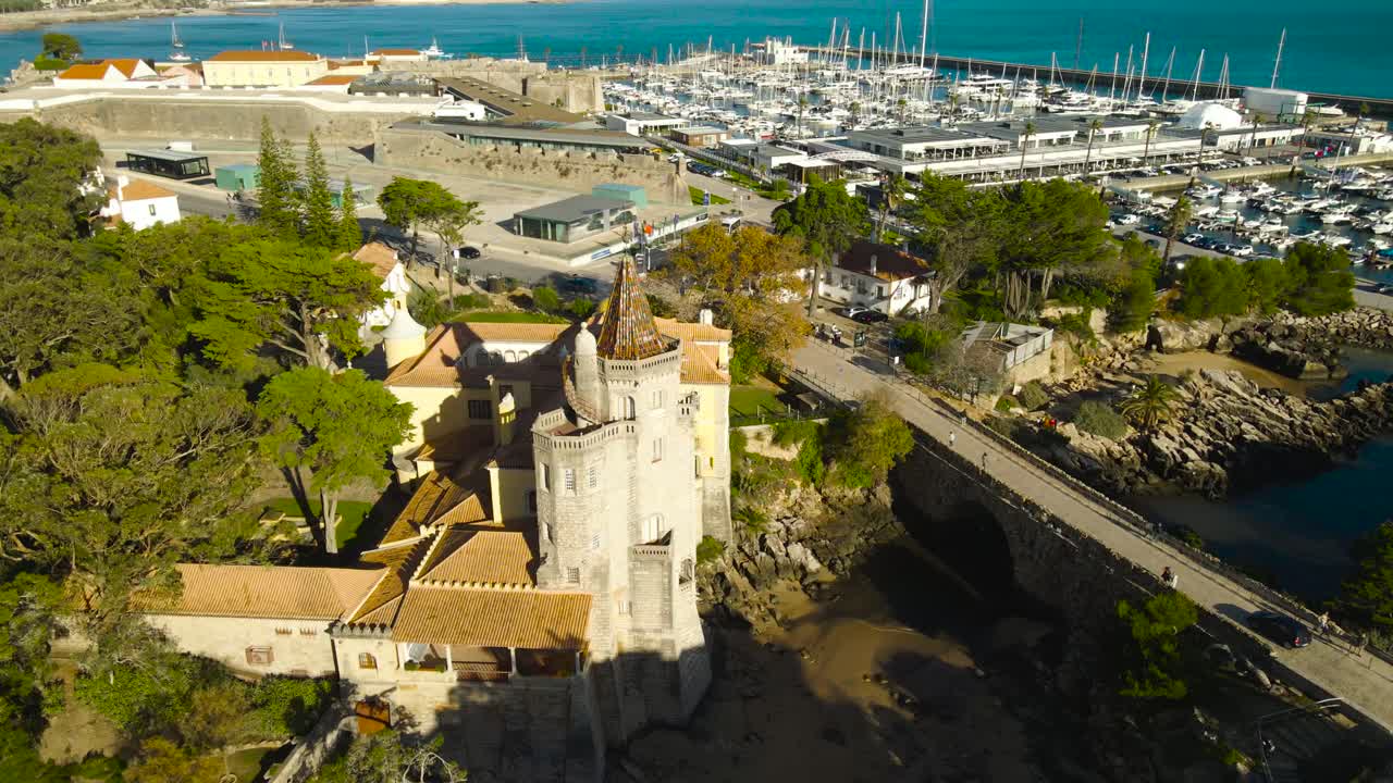 Aerial drone video flying around gorgeous Condes de Castro Gumaraes museum and library in Estroil Cascais Portugal during a sunny day with Casa de Santa Maria and Ocean in the background, Yacht harbor