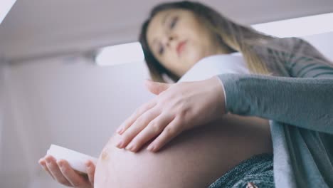 pregnant woman applies cream stroking large tummy close view