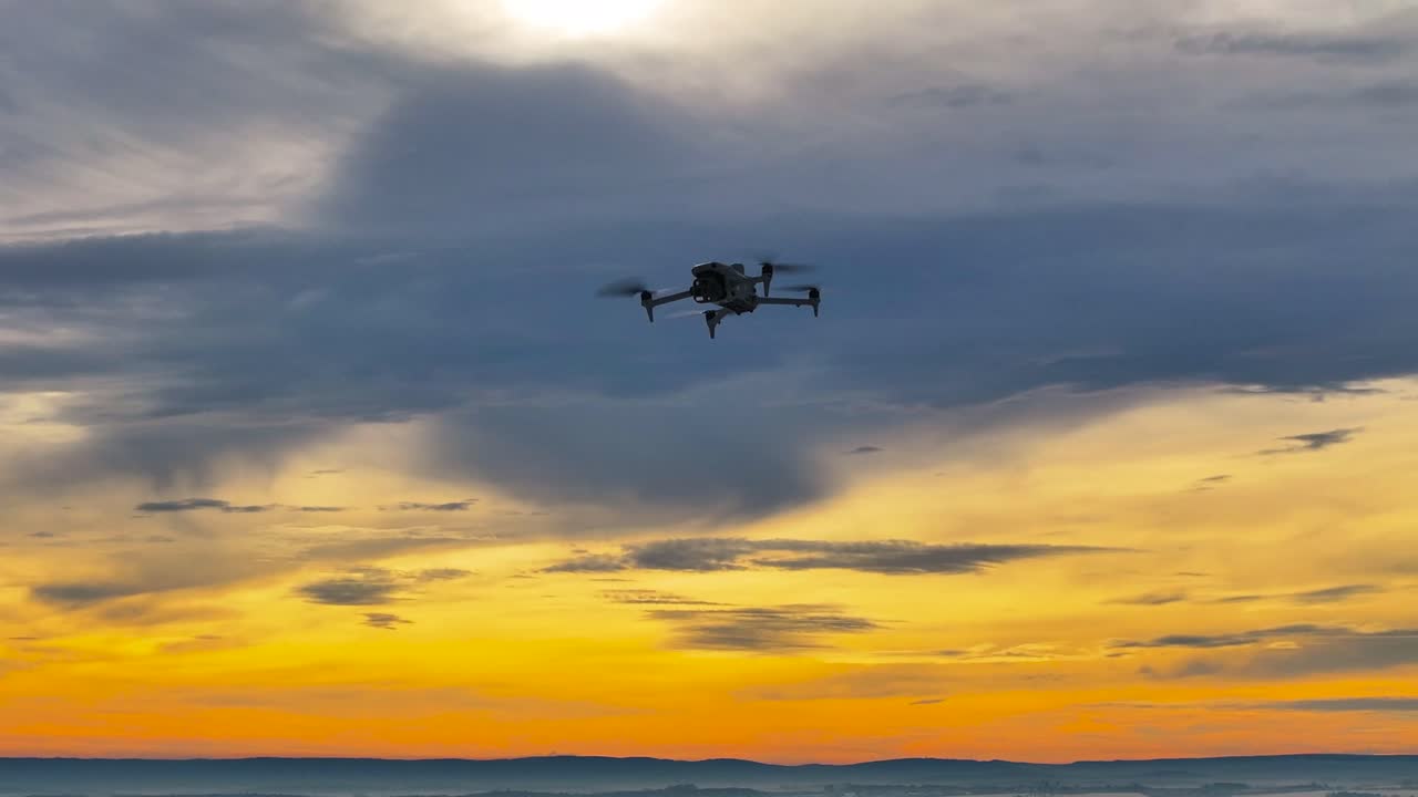 Drone silhouette flying against dramatic sunset with gold and blue sky, Czechia