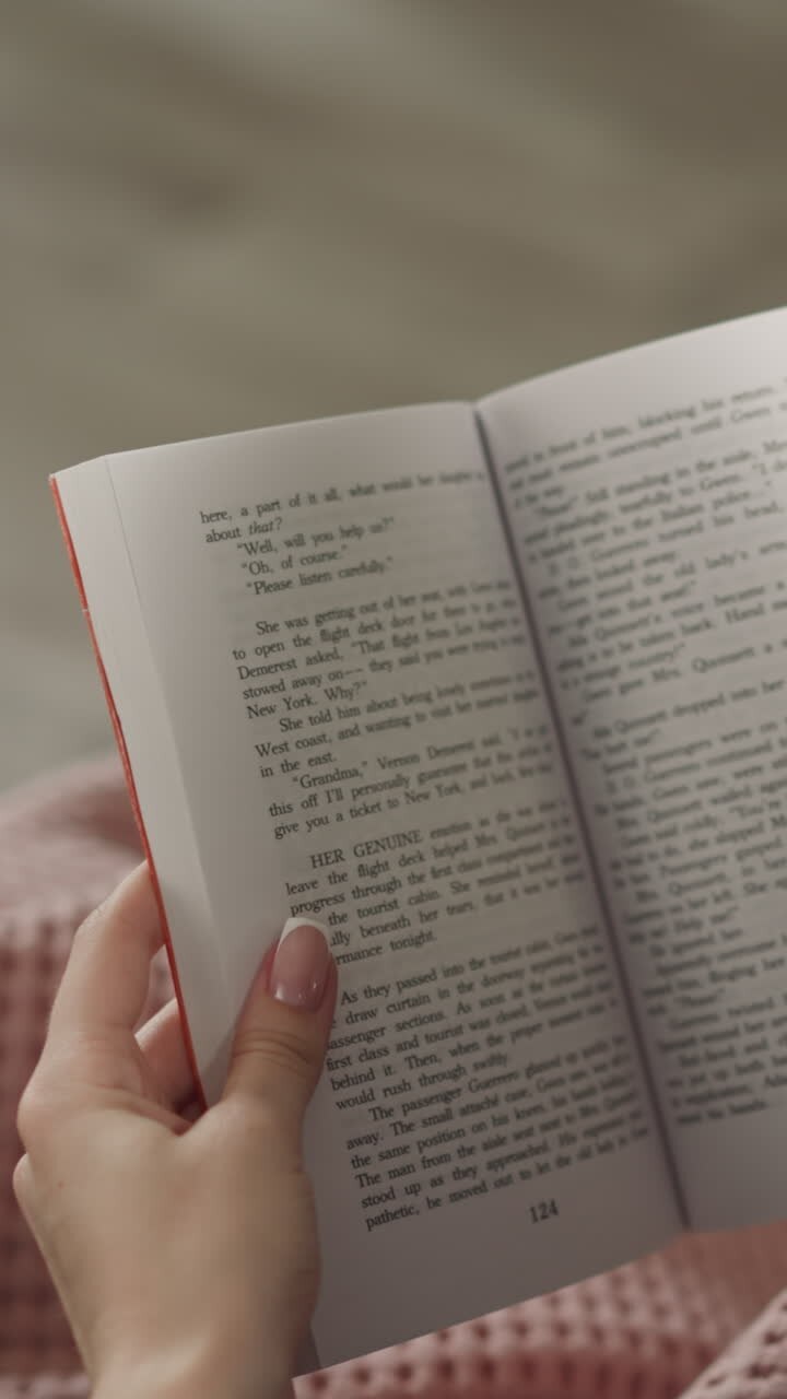 Redhead woman flips pages reading interesting story at home after work. Hands of female reader holding English book on blurred background close rear view