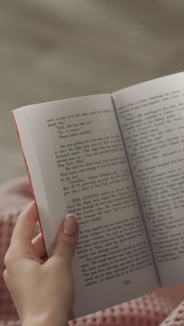 redhead woman flips pages reading interesting story at home after work. hands of female reader holding english book on blurred background close rear view