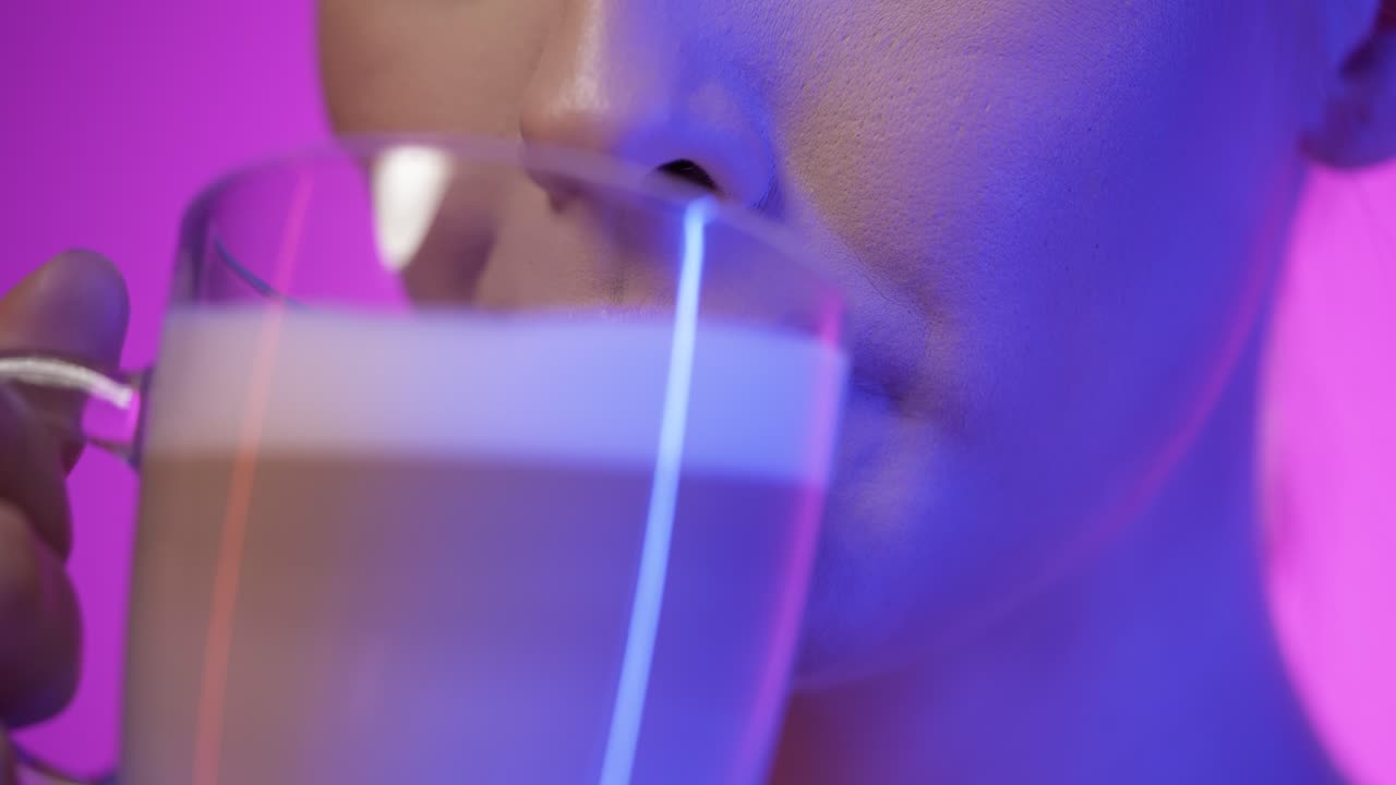 Close up of a pretty woman while enjoying a vegan freshly brewed coffee latte macciato or cappuccino in the morning for breakfast and smiling happily in front of purple background in slow motion