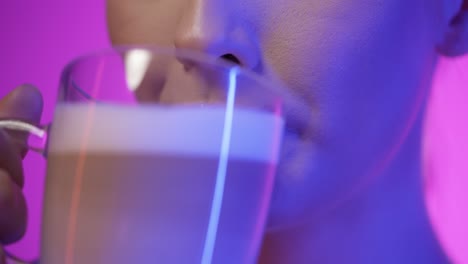 Close-up-of-a-pretty-woman-while-enjoying-a-vegan-freshly-brewed-coffee-latte-macciato-or-cappuccino-in-the-morning-for-breakfast-and-smiling-happily-in-front-of-purple-background-in-slow-motion