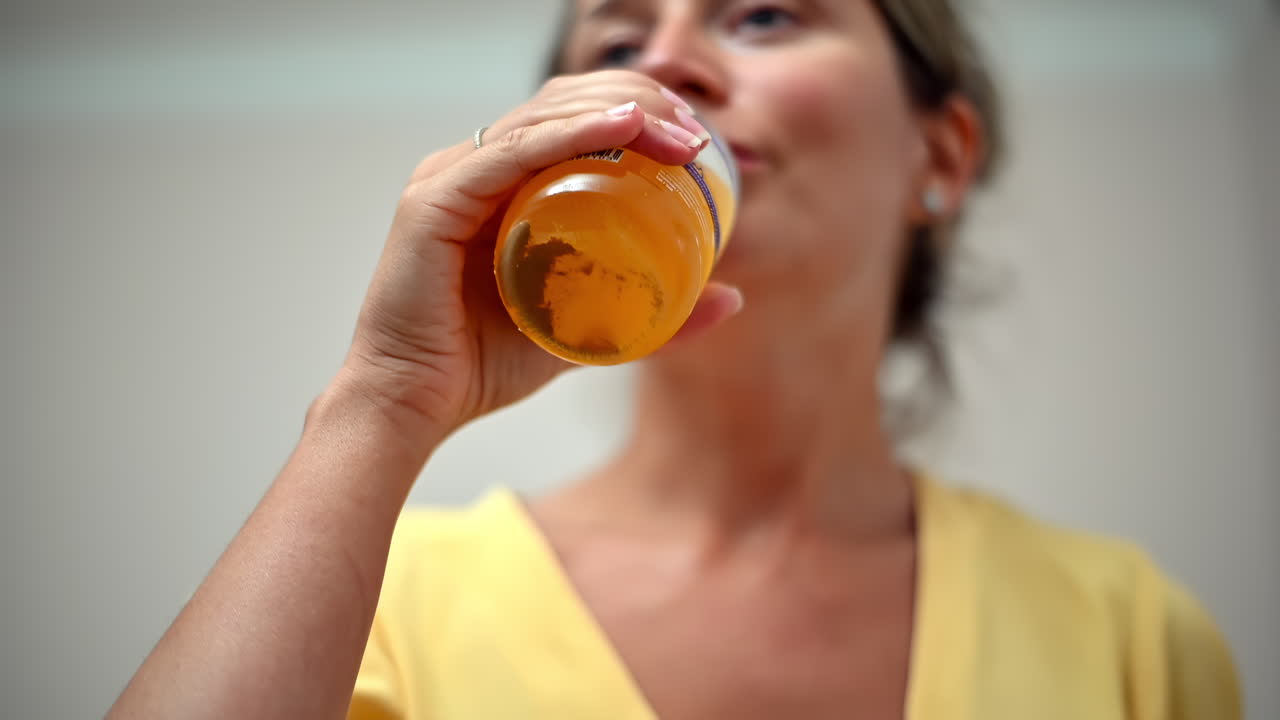 Una donna sorseggia una bevanda fresca da un bicchiere, sorridendo dolcemente mentre si gode il suo drink in una stanza ben illuminata. L'atmosfera è calma e invitante.