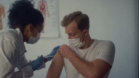 african nurse injecting vaccine in man shoulder. doctor vaccinating patient.