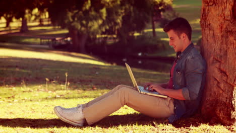 Un-Joven-Sentado-Contra-Un-árbol-Y-Usando-Su-Computadora-Portátil.