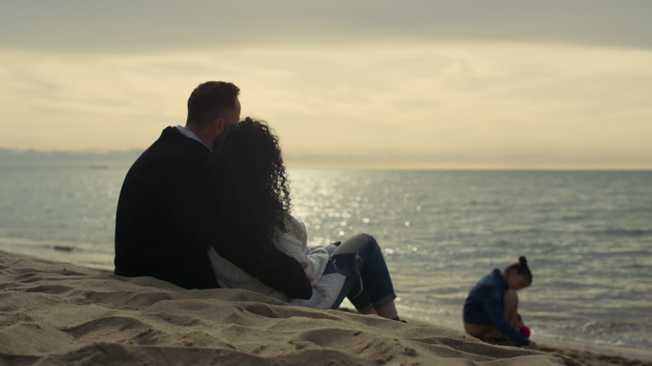 Famiglia che guarda il tramonto in spiaggia durante le vacanze al mare. Le persone si godono il tempo sulla riva.