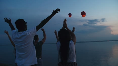 grupo de amigos despidiéndose con un gesto de las linternas que vuelan en el cielo por la noche