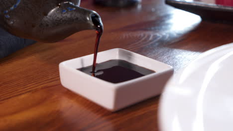 hand pours soy sauce from handmade clay pot into small dipping dish, 4k