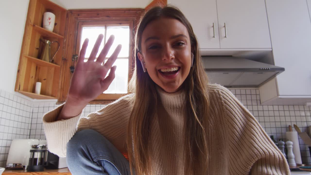 retrato de una mujer sonriendo y saludando mientras está sentada en la cocina