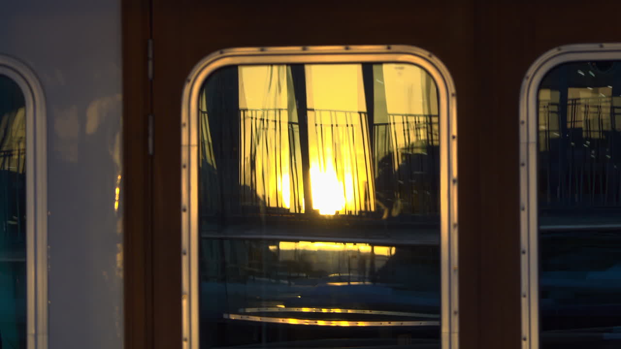 Close-up of a yacht's window reflecting the golden sunset and marina railings in Cannes