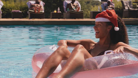 mujer en vacaciones de navidad flotando en un anillo inflable en la piscina con sombrero de papá noel