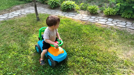 smiling toddler pushes his feet from the ground to move his toy car. lovely kid having active tie outdoors in summer. top view.