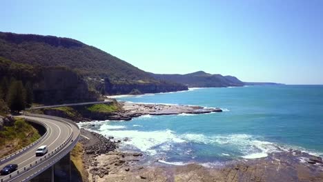 Las-Imágenes-Aéreas-De-Un-Impresionante-Puente-Largo-Y-Curvo-Junto-Al-Mar-Resaltan-El-Gran-Paseo-Pacífico-Con-El-Océano-Pacífico-Sur-Y-La-Vista-Del-Cielo-Azul-En-Un-Día-Soleado,-Sydney,-Australia