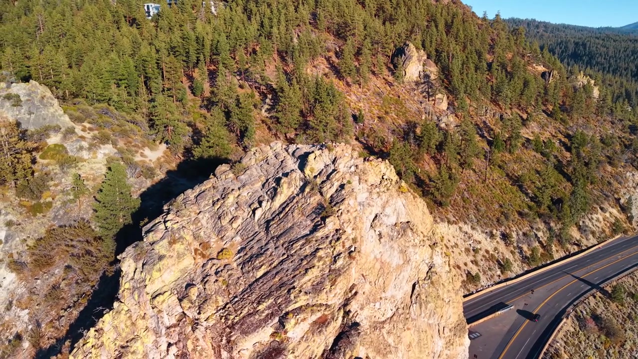 Cave Rock -kallio Nevadan valtatien varrella. Auringonvalo paljastaa vaalean jyrkänteen harjanteet, ja rinteellä näkyy asfalttitien liikennettä sekä havupuita.