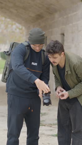 two men reviewing photos on a camera outdoors