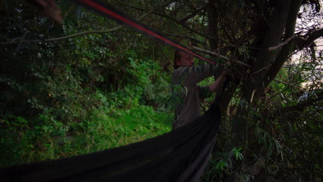 hombre tira y aprieta la línea a través de los árboles para asegurar la hamaca en el área forestal ribereña