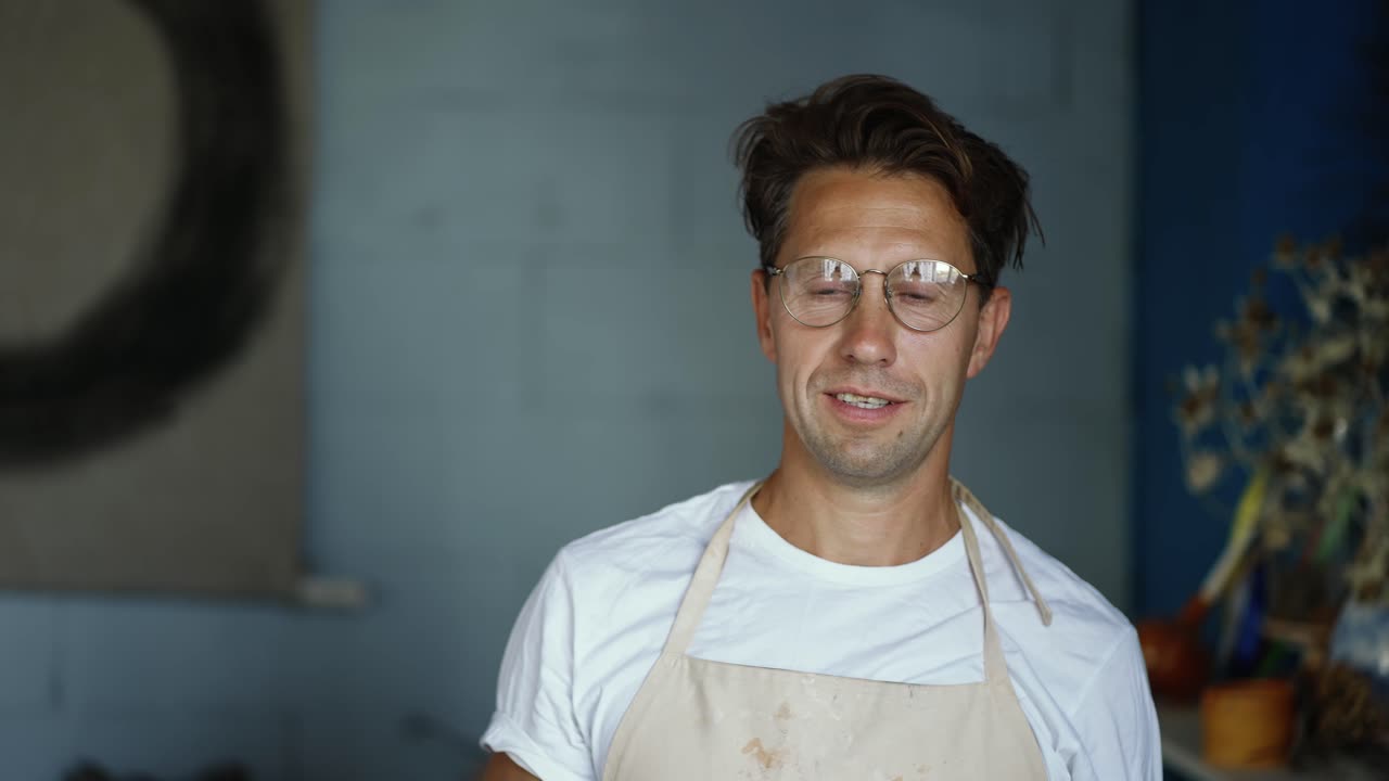 Portrait of a young happy potter posing and putting on glasses. close-up video