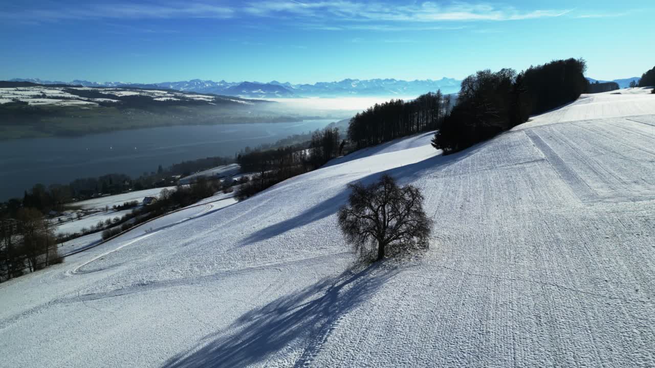 Aerial of a snow covered landscape in central Switzerland revealing a lake and the Alps in the background