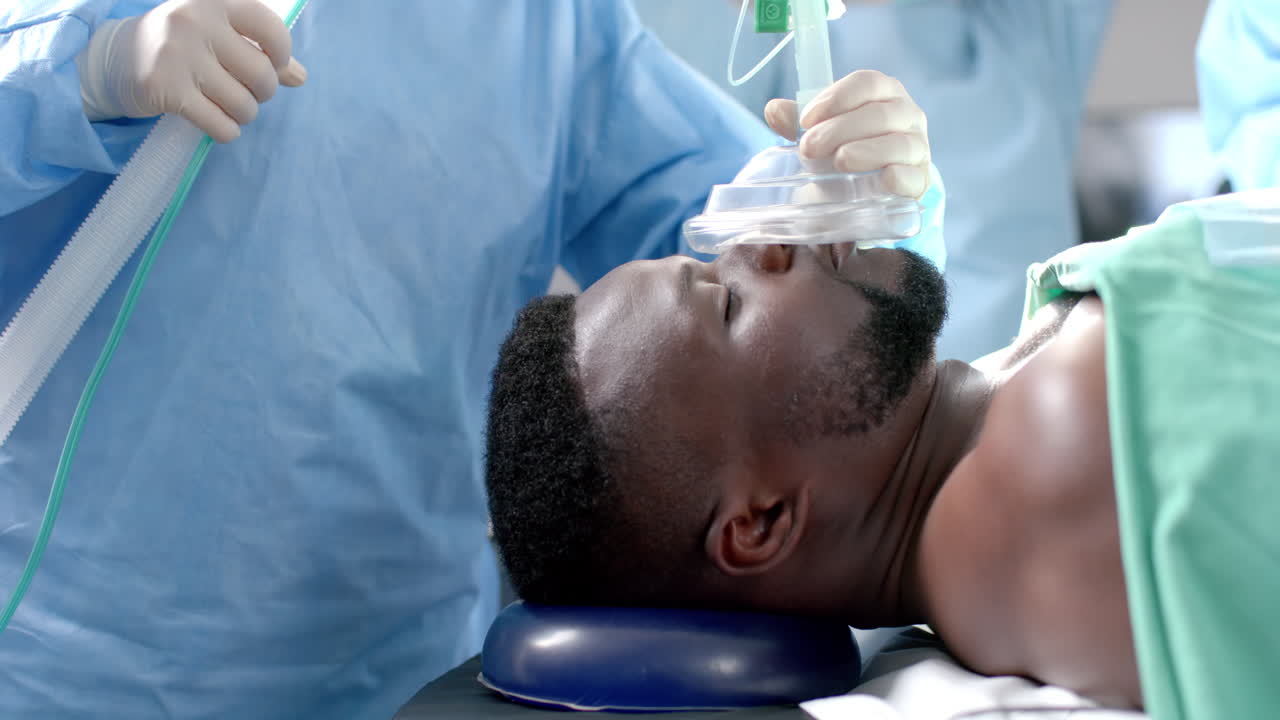cirujano aplicando una máscara anestésica a un paciente afroamericano en el quirófano, cámara lenta