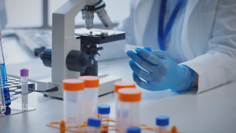 primer plano de un trabajador de laboratorio que lleva a cabo investigaciones utilizando un microscopio con un tubo de ensayo etiquetado como tau