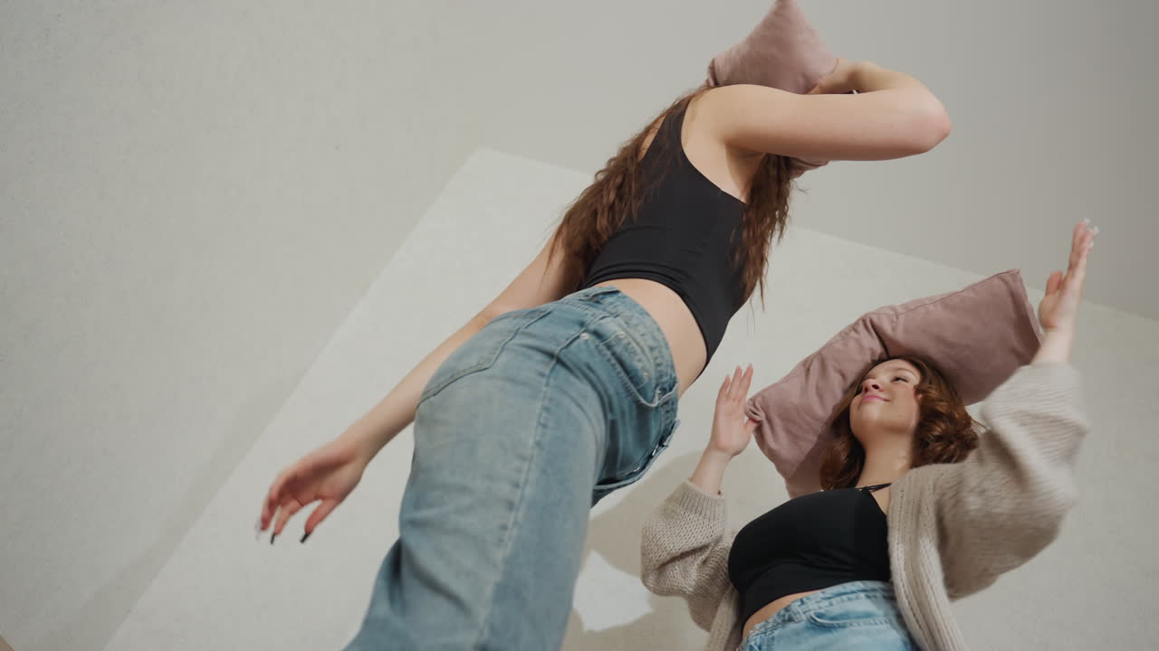 Dynamic Lowangle Shot Of Friends Playing, Lively Bedroom Scene Capturing Energetic Pillow Battle Moments, Two Friends In Lively Interaction With Flying Cushions In Spirited Bedroom Setting
