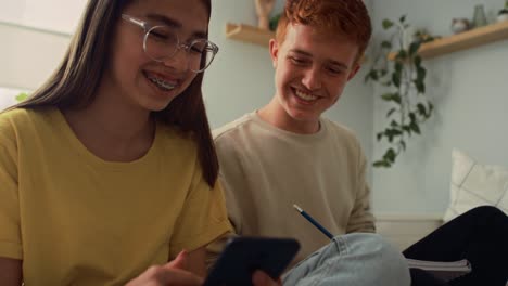 Two-caucasian-teenagers-sitting-on-floor-and-learning-from-books-and-laptop