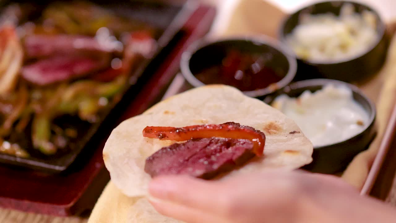 Hand places grilled beef and salsa on tortilla, warm lighting, close-up, shallow depth of field