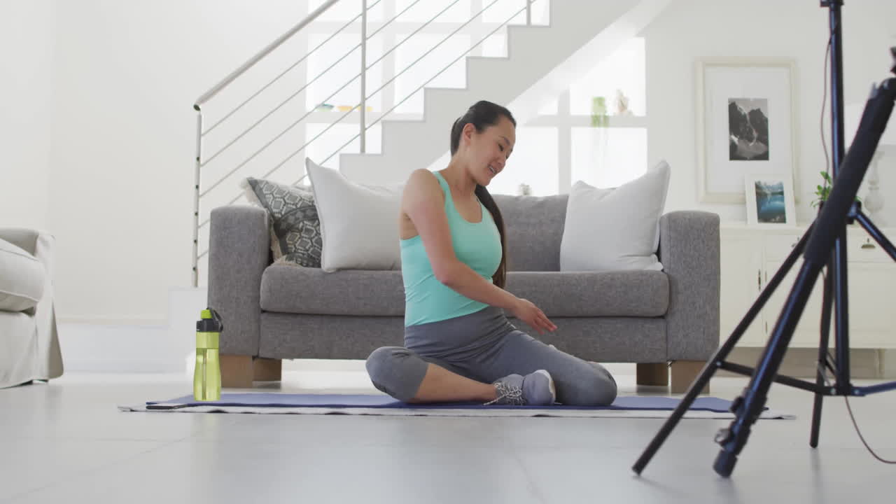Stretching on yoga mat, woman in living room with exercise equipment nearby