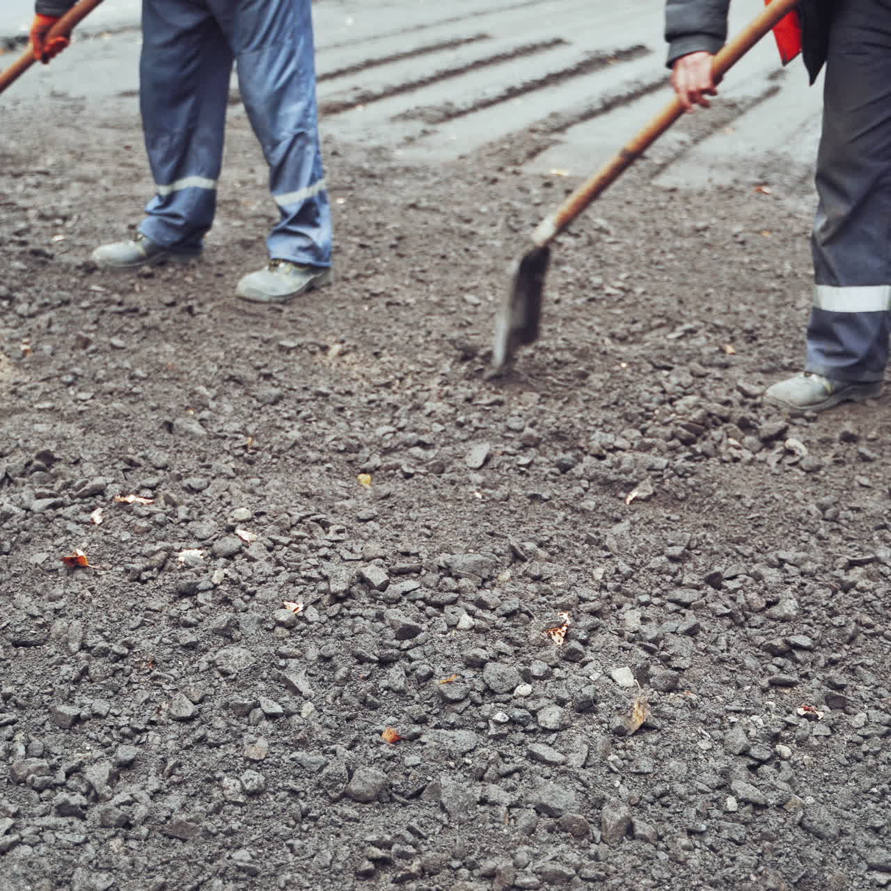 Workers in uniform with shovels during road street repairing works. Street resurfacing. Fresh asphalt construction. Close-up