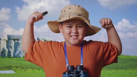 asian boy with a hat and binoculars using the magnifying glass then flexing his bicep while traveling in stonehenge. boy researcher examines something, travel tourism adventure, close up