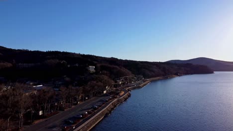 coastal road curving along a calm bay with hills, clear sky at dusk, aerial view