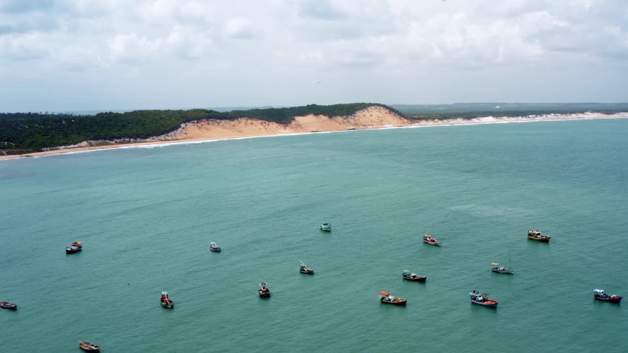 toma aérea giratoria de un grupo de pequeños barcos de pesca atracados cerca de la playa de cacimba con dunas de arena en el fondo en la famosa ciudad costera de baia formosa en rio grande do norte, brasil