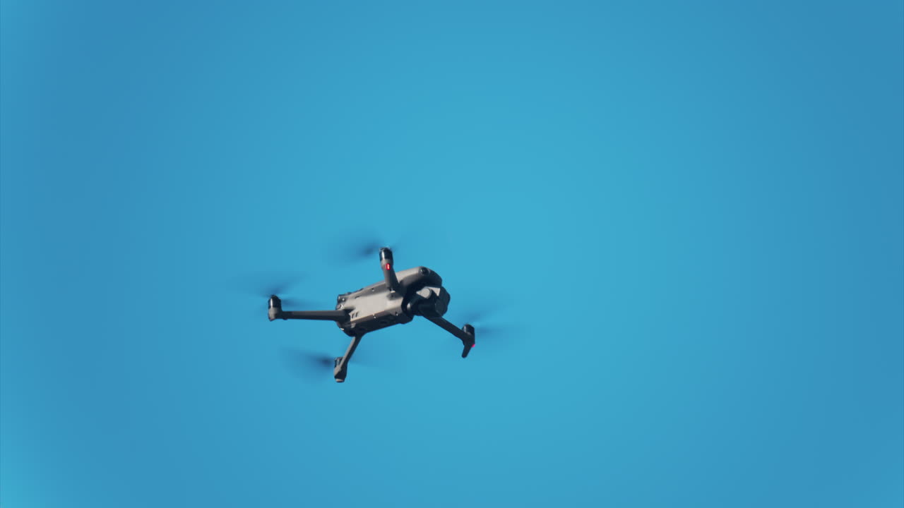 Low angle view of a drone hovering against a vivid blue sky