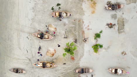 top view of fishermen repairing fishing nets next wooden canoes in kuakata sea beach, bangladesh