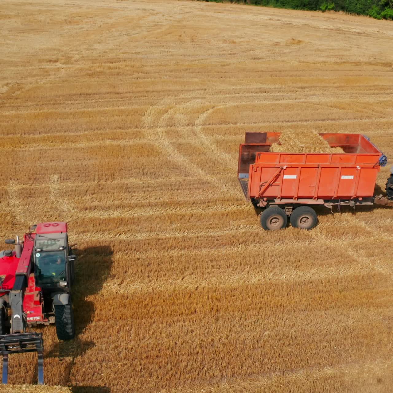 Big tractor machine being loaded with straw. Skid loader picks up two hay bales piled on one another. Aerial view
