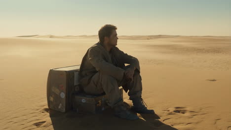 man sits alone on a suitcase in a sprawling desert landscape