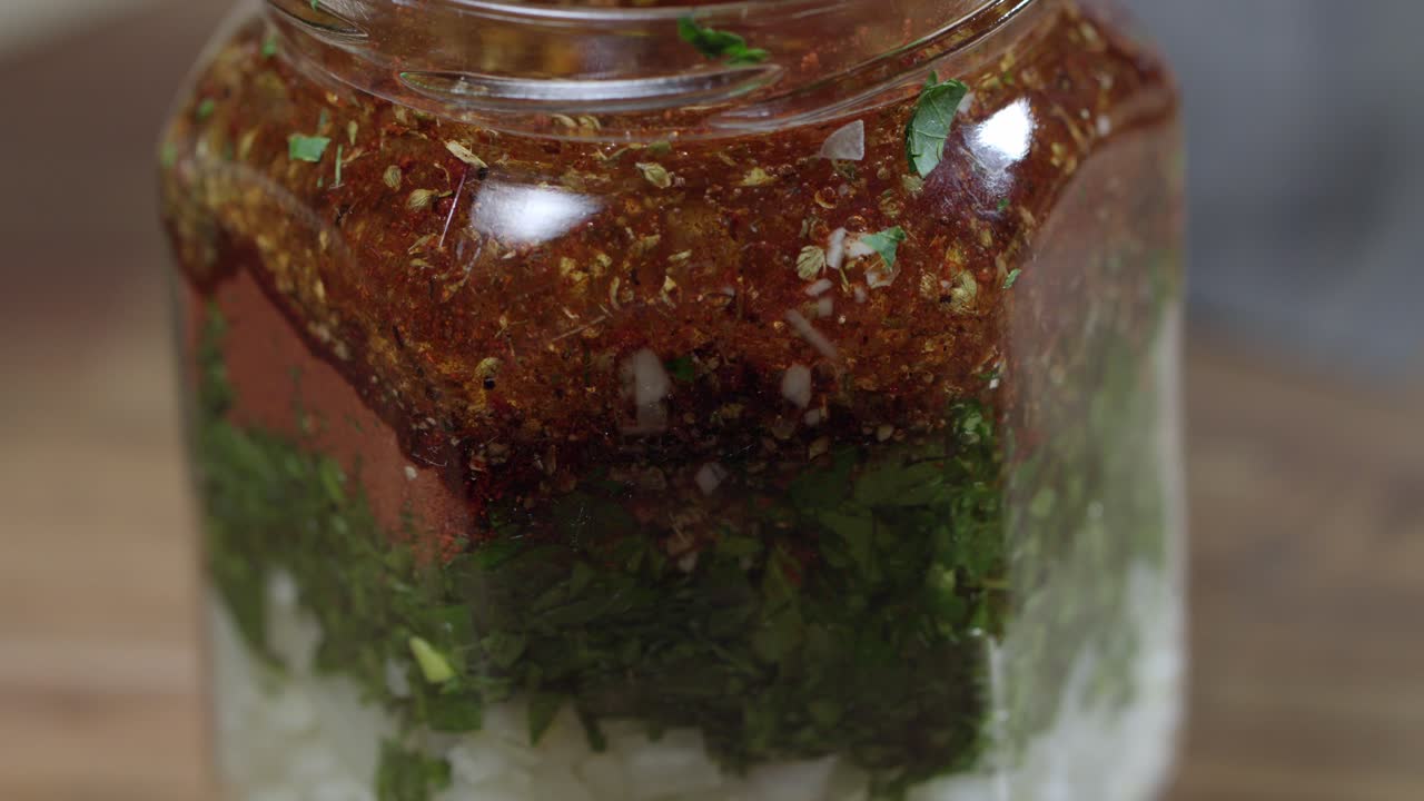 frasco de vidrio con ingredientes para chimichurri, perejil fresco, orégano, pimienta roja molida, pimienta negra, sal, ajo y más