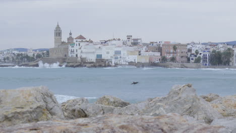 surfers floating in big waves near ancient coastal town during stormy morning