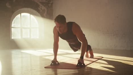 Male-athletes-in-black-sportswear-summer-uniform-doing-push-ups-using-special-hand-rests-on-a-red-mat-in-a-sunny-brick-hall