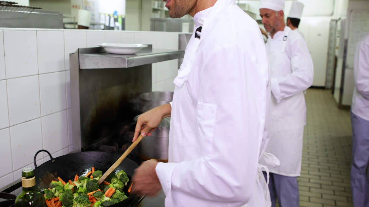 chef sonriente freyendo verduras en un wok y añadiendo aceite