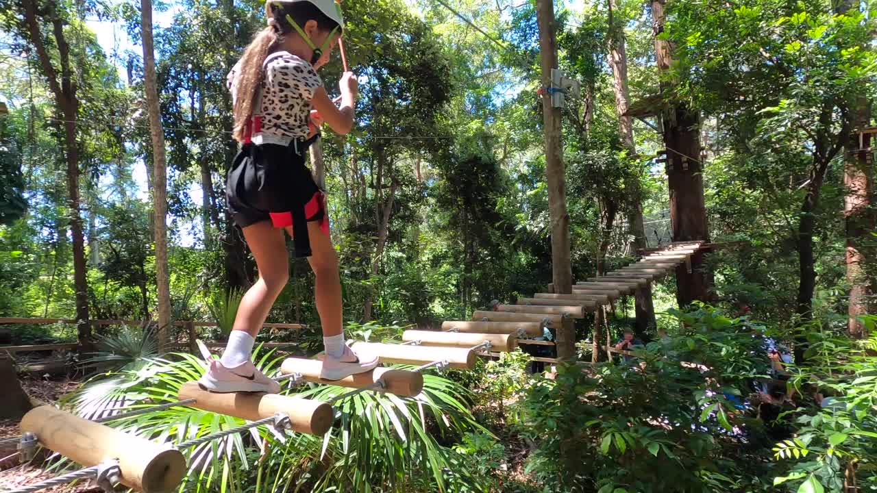 un niño pequeño balanceándose y caminando a través de un puente de cuerda de carrera de obstáculos