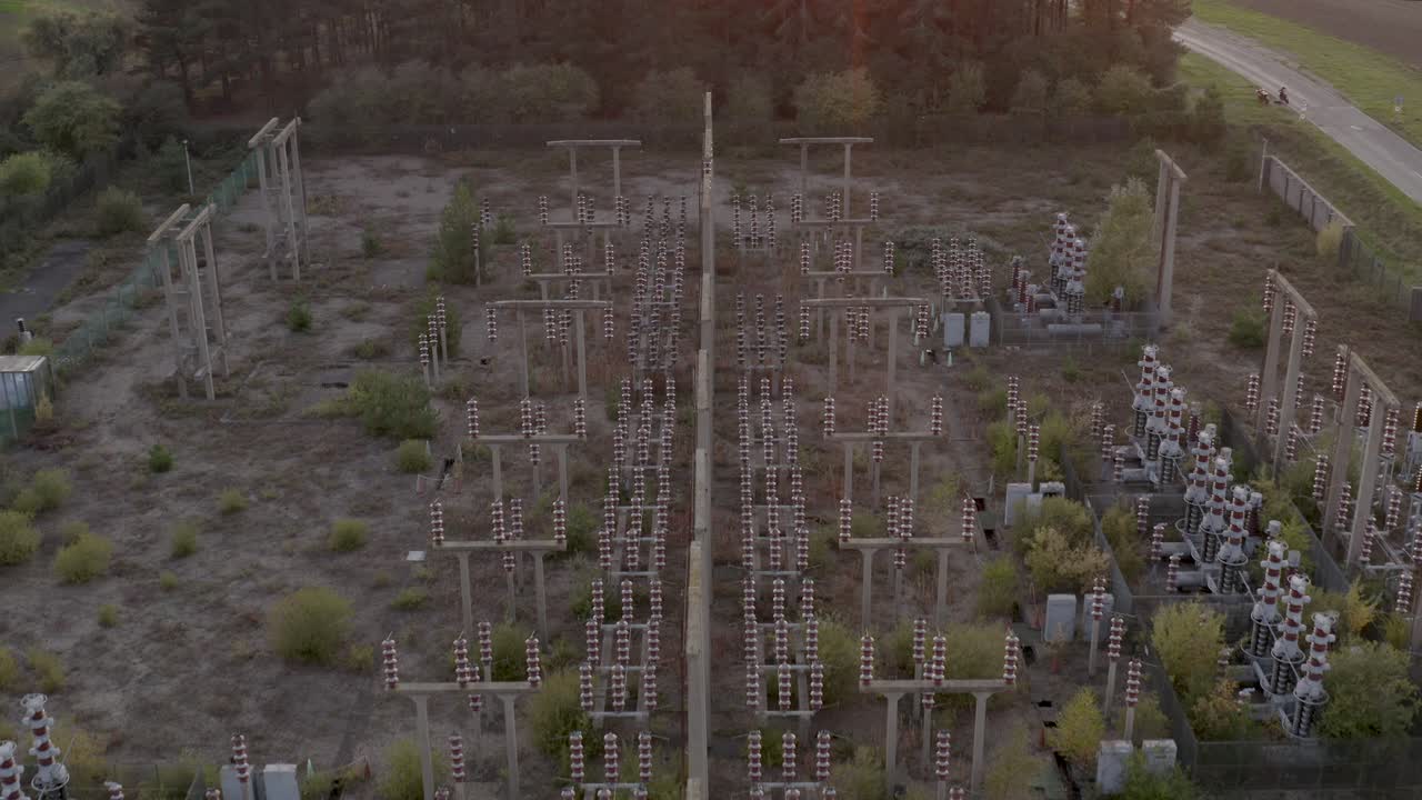 Nature regrowth around a derelict power station in the countryside at sunset with lens flare. Fly over.